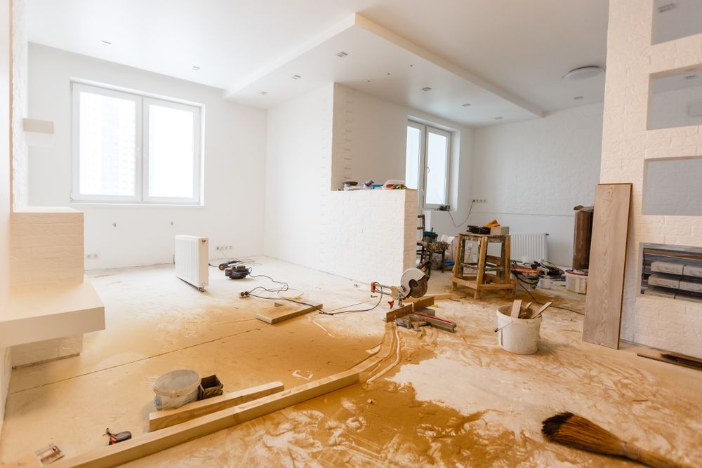 Man in white work clothes and hard hat, sanding a wall with a power sander, indoors.